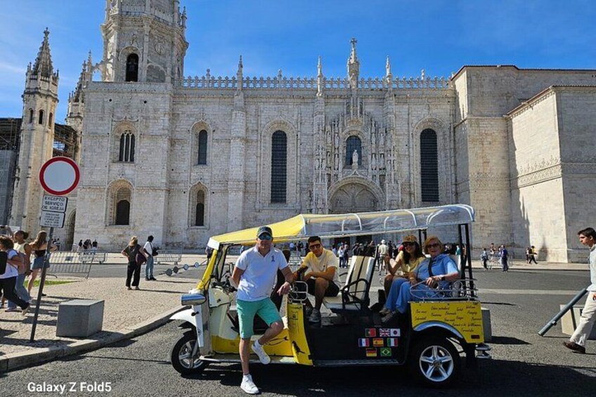 A historic cathedral with intricate architecture, a yellow and white vehicle with passengers, and a clear blue sky. 2