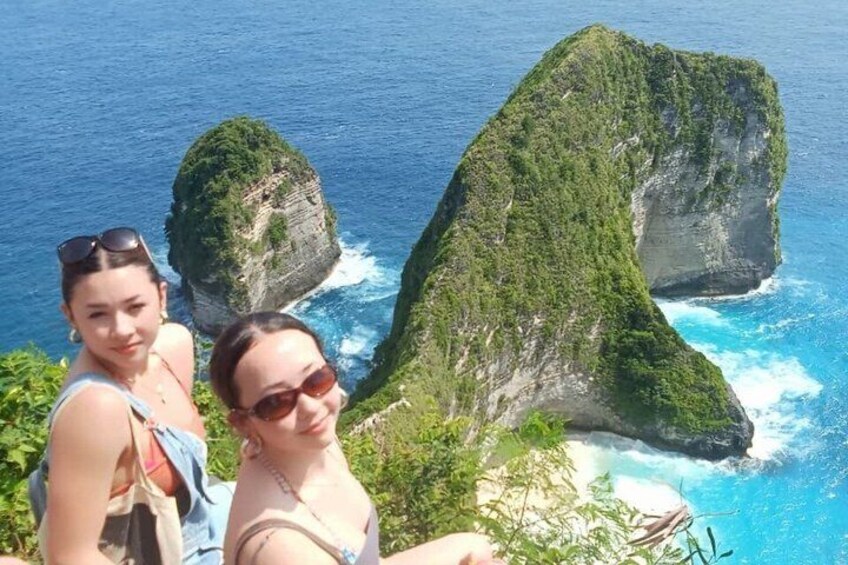 Two people taking a photo with a large rock formation and the ocean in the background. 1