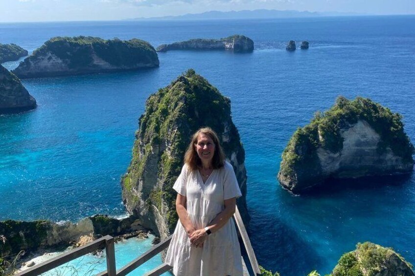 A person standing on a wooden deck overlooking a coastal landscape with clear blue waters and green islands. 3