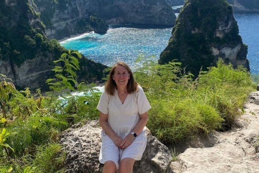 A person sitting on a rock by a coastal cliff with a view of the ocean and greenery. 5