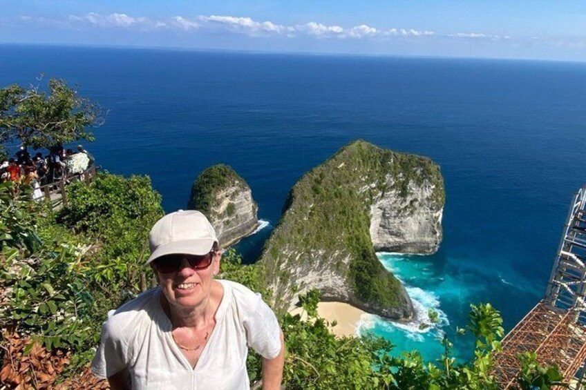 A person standing on a cliff overlooking a coastal landscape with a large rock formation and the ocean. 2