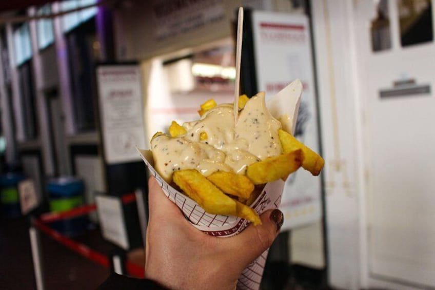 A hand holding a paper container with French fries topped with a creamy sauce. 5