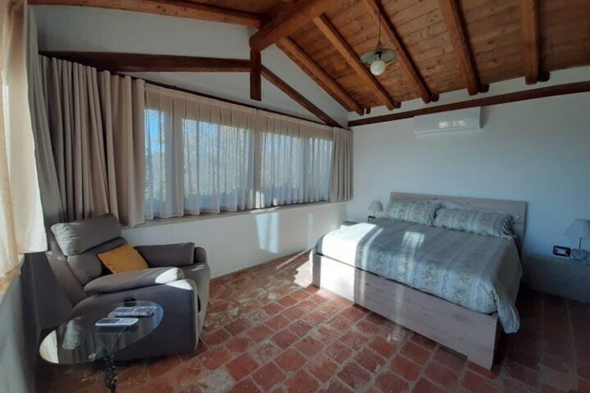A bedroom with a bed, a chair, a table, and a window with curtains. 3