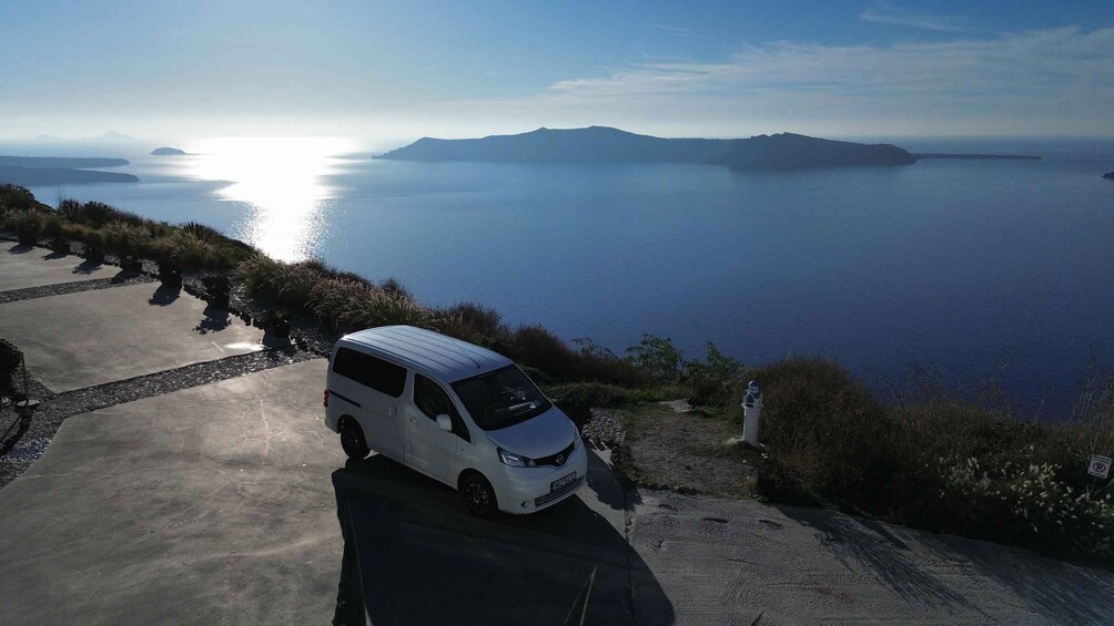 A white van parked on a coastal road with a scenic view of the sea and distant mountains. 3