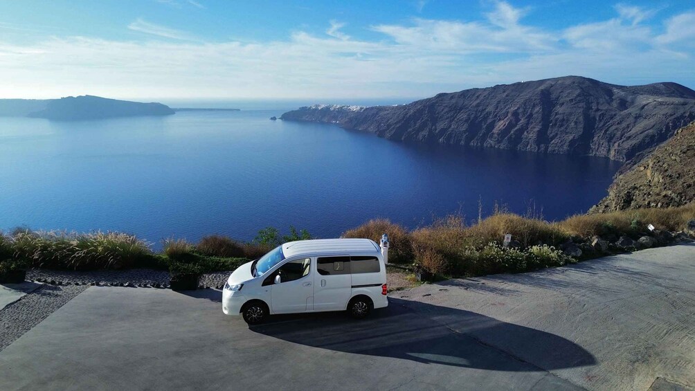 A white van parked on a coastal road with a view of a large body of water and mountains in the distance. 4