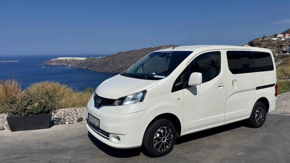 A white van parked on a coastal road with a clear view of the sea and rocky hills in the background. 5