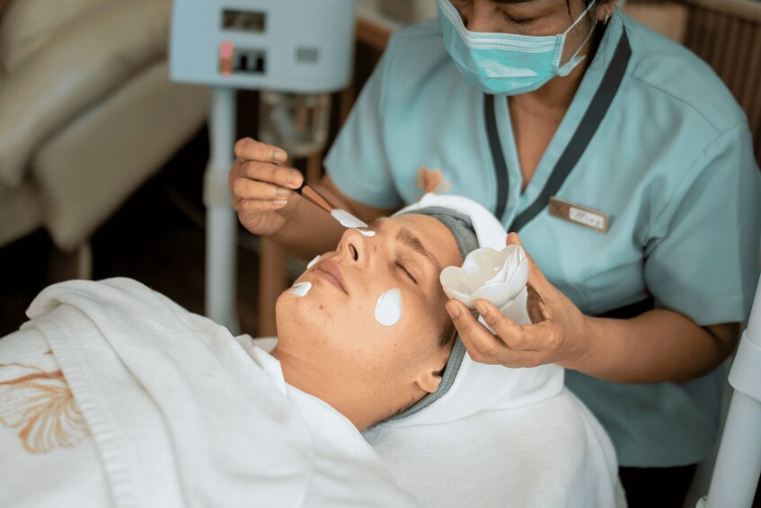 A person receiving a facial treatment with a facial mask and a cotton pad. 4