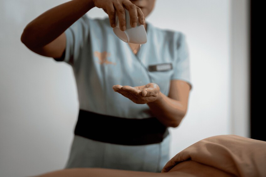 A person in a light blue uniform pouring a liquid from a white container into their hand. 5