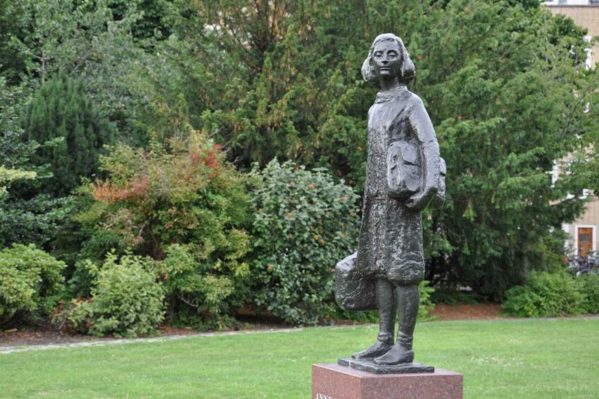 A statue of a woman in a dress on a pedestal in a park with trees and grass. 3