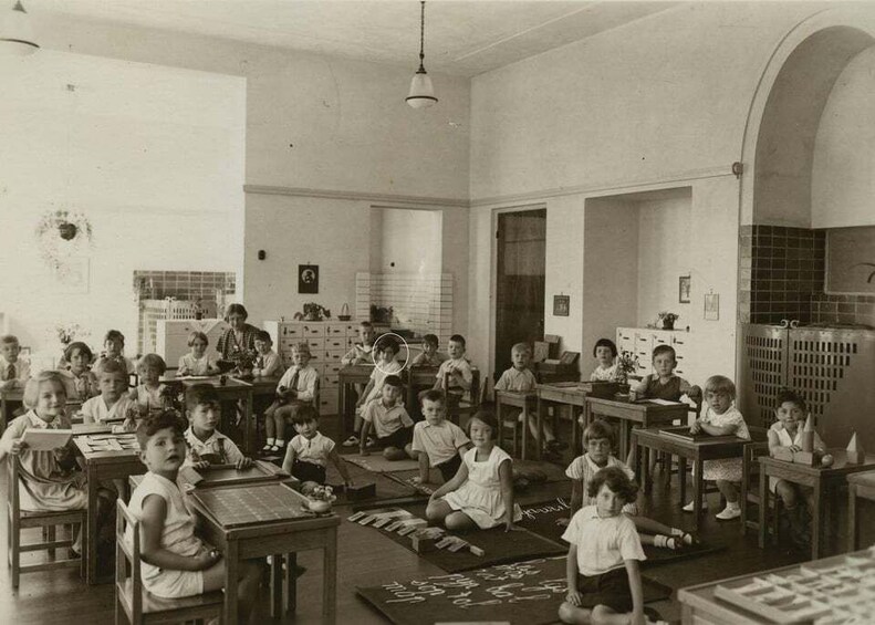 A classroom with children seated at desks, engaged in various activities. 5