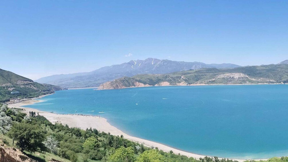 A coastal landscape with a clear blue sea, sandy beach, and mountainous terrain. 5