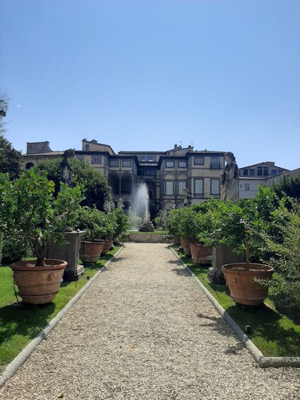 A courtyard with a gravel path, potted trees, and a fountain. 5