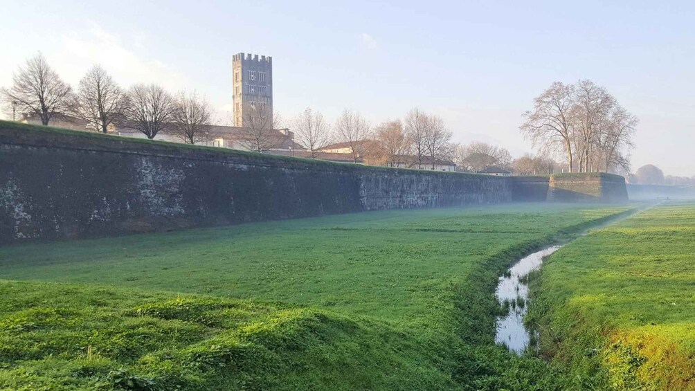 A grassy field with a stream, a stone wall, and a tower in the distance. 4