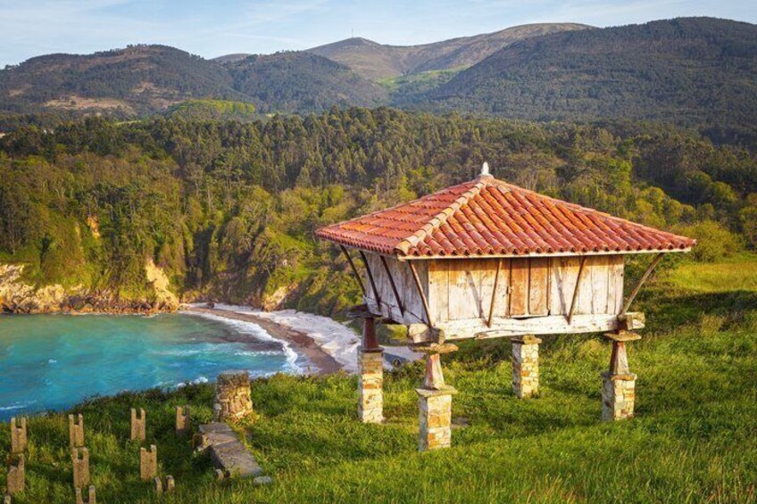 A wooden gazebo with a red roof on a grassy hill overlooking a beach and forested mountains. 2