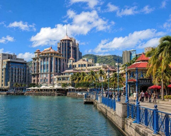 A waterfront promenade with buildings, palm trees, and a clear blue sky. 2