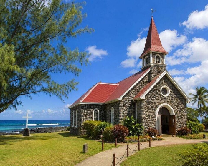 A stone church with a red roof and a cross in front, located near a beach. 4