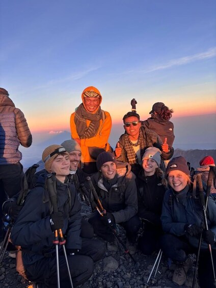 A group of people on a mountain with a sunset in the background. 4