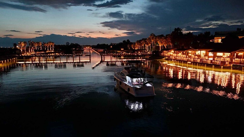 A boat on calm water, a lit bridge, and buildings reflecting on the water at dusk. 5