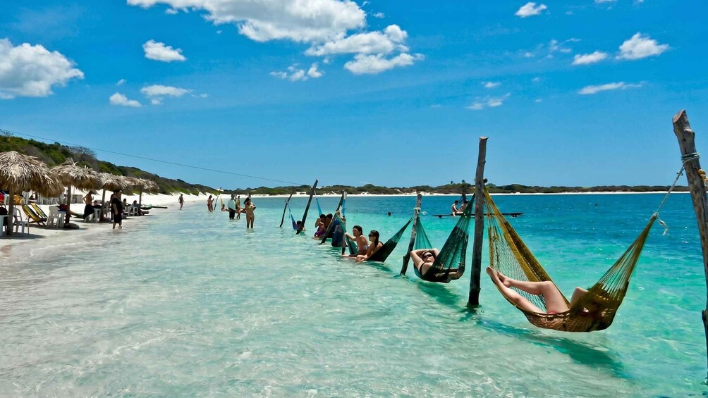 A beach with clear turquoise water, people relaxing in hammocks, and thatched umbrellas. 5