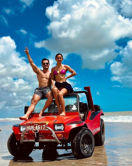 A red off-road vehicle on a beach with a clear sky and ocean in the background. 1