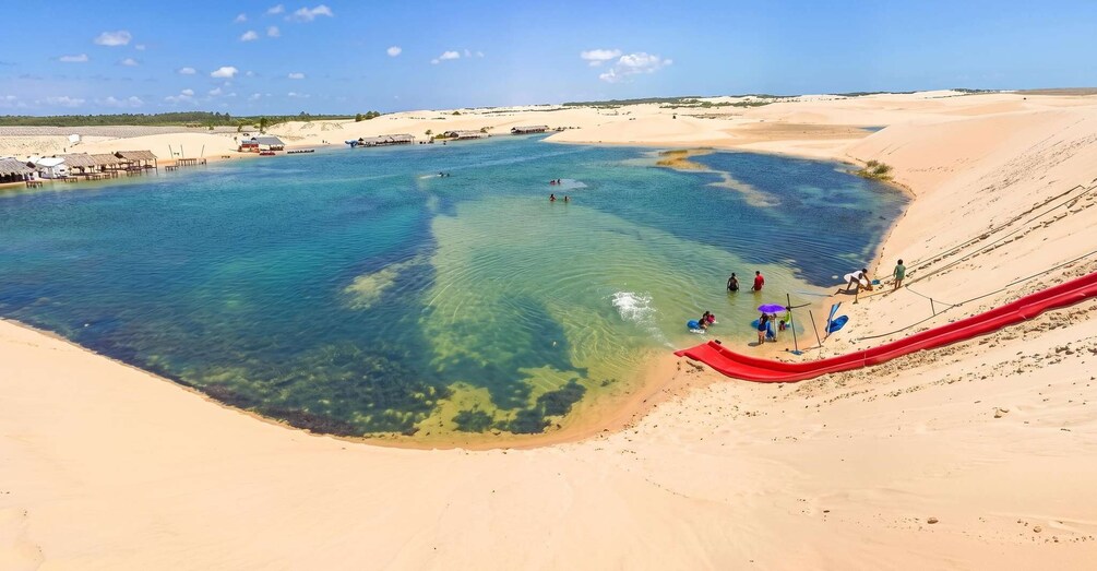 A beach with clear water, a red slide, and people swimming. 4