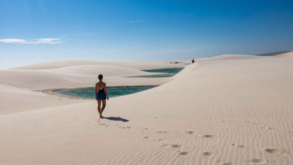 A person walking on sand dunes with a body of water in the background. 2