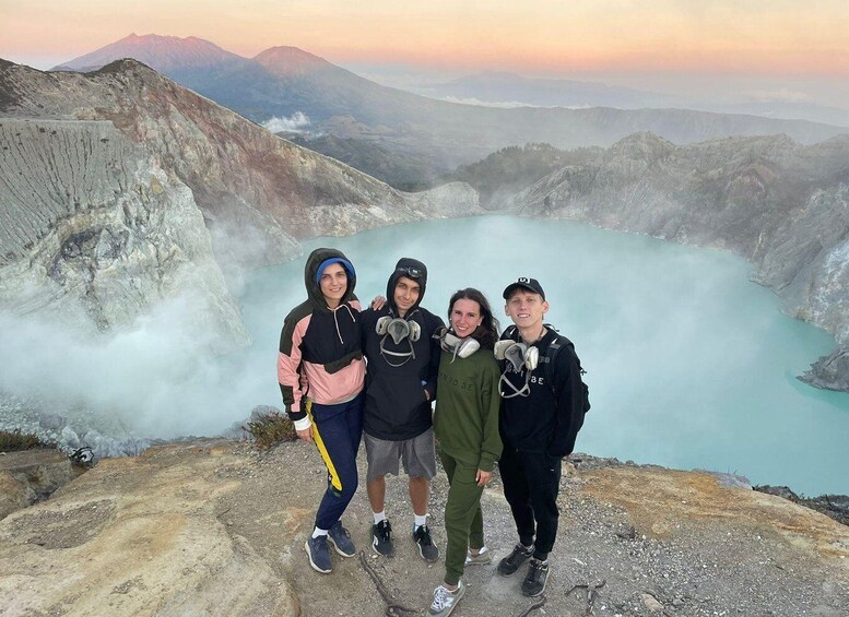 Four people standing on a rocky outcrop with a lake and mountains in the background. 2