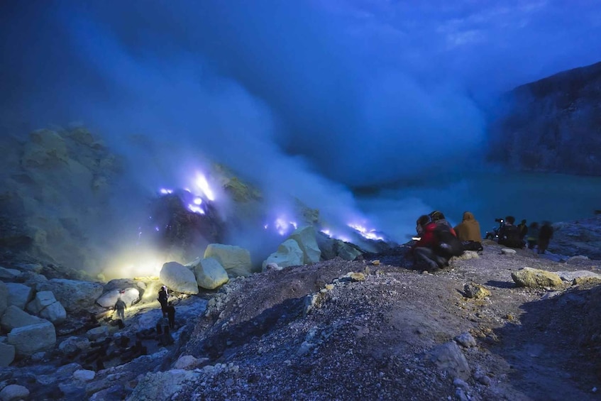 People sitting on rocks near a geothermal area with steam and glowing rocks. 1