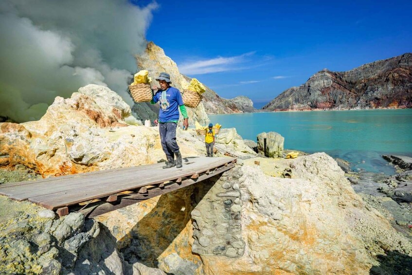 A rocky landscape with a wooden bridge, a person carrying bags, and a child nearby. 3