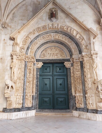 A detailed stone doorway with a green door, surrounded by ornate carvings and a pointed arch. 3