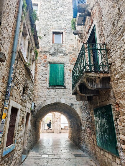 A narrow alleyway with stone buildings, a green door, and a metal balcony. 4