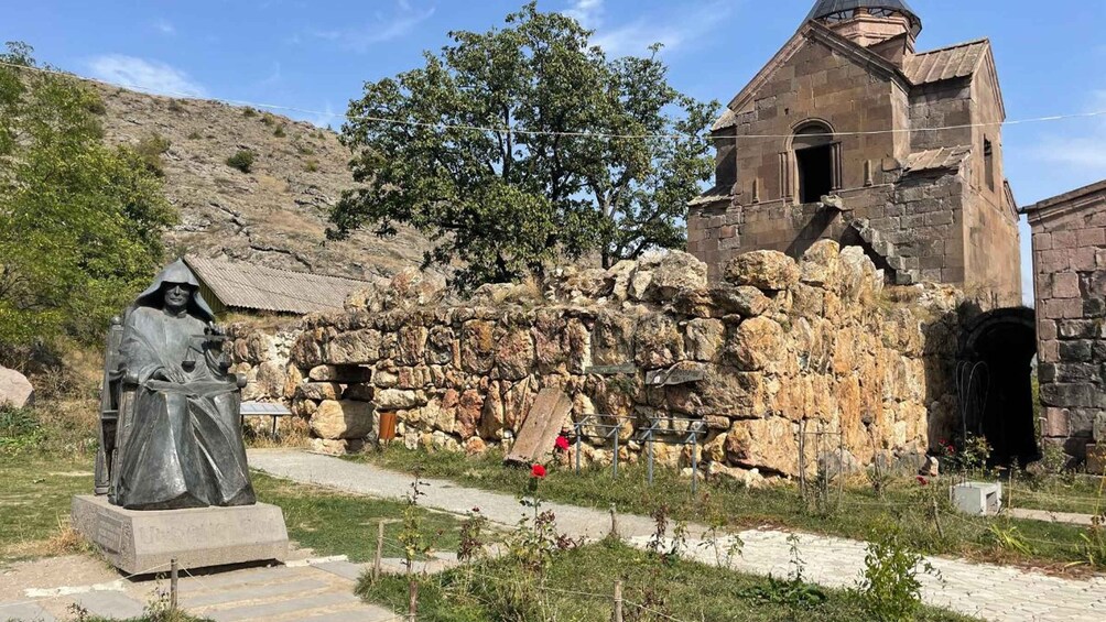 A statue of a robed figure, a stone wall, and a church with a bell tower. 5
