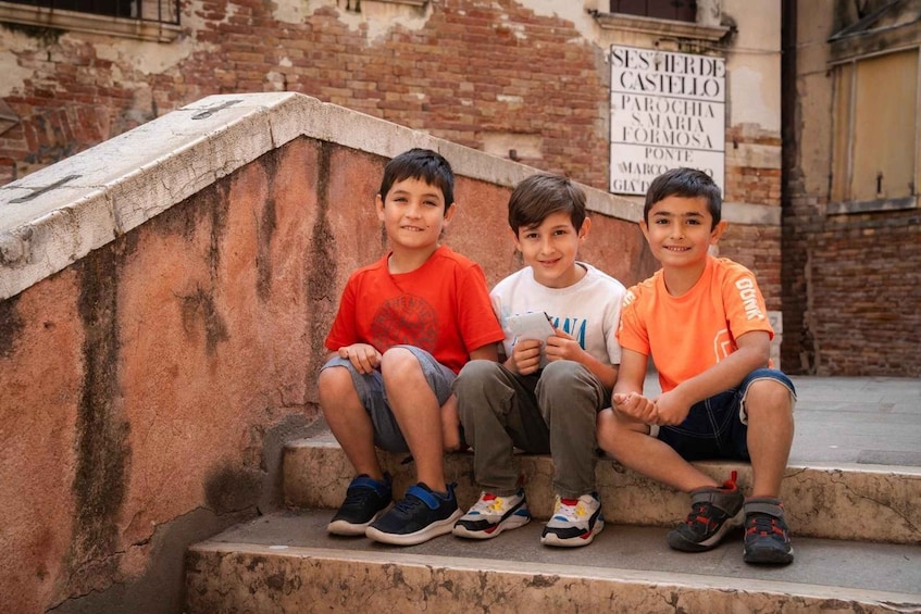 Three children sitting on steps in front of a building with a sign that reads 'SESER DE CASTELLO.' 3