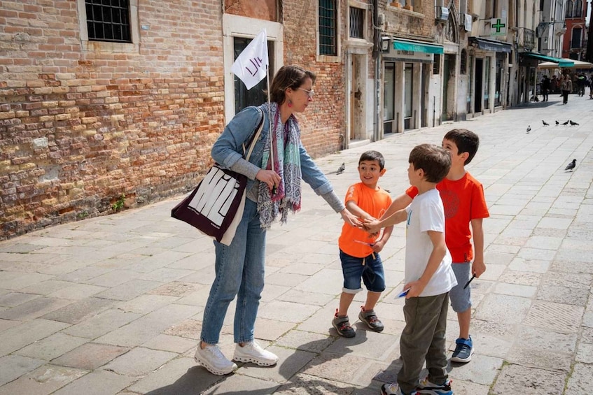 A woman with a flag, three children, and pigeons on a city street. 1