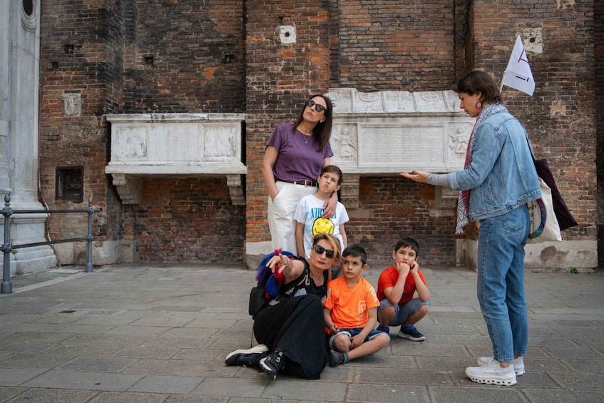 A group of people in an outdoor setting with a brick wall and a white monument in the background. 4
