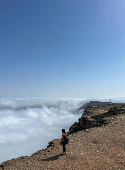 Una persona in piedi su una scogliera rocciosa con vista su una vasta vallata avvolta dalle nuvole. 1