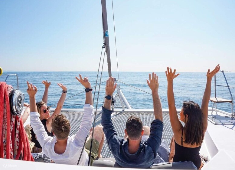 A group of people on a sailboat with their hands raised, enjoying the sea view. 1