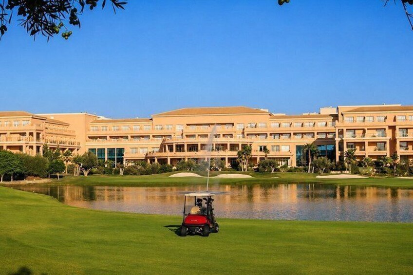 A golf course with a red cart, a pond, and a hotel building in the background. 3