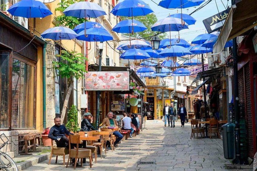 A street with outdoor seating, blue umbrellas, and people walking. 5