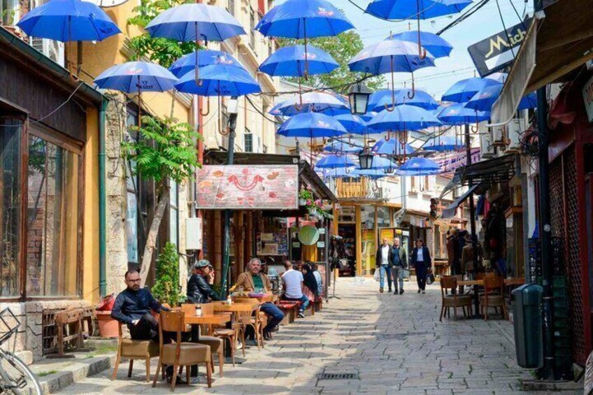 A street with outdoor seating, blue umbrellas, and people walking. 5