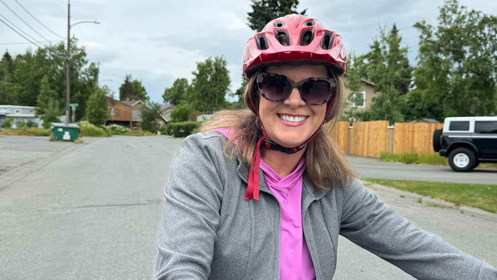 A person wearing a helmet and sunglasses, riding a bicycle on a residential street. 3