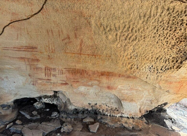 A cave wall with ancient petroglyphs and a large boulder at the bottom. 1