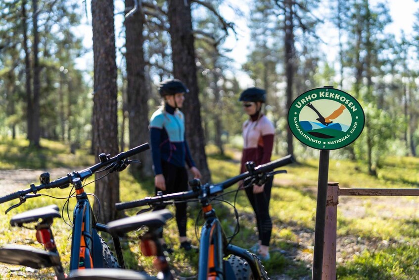 A forested area with a sign for Urho Kekkonen National Park and bicycles parked. 3