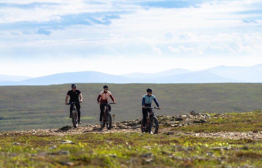 Three cyclists on a rocky trail with a mountainous landscape in the background. 4