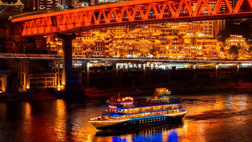 A brightly lit riverboat with a traditional Chinese roof, a red bridge, and illuminated buildings in the background. 2