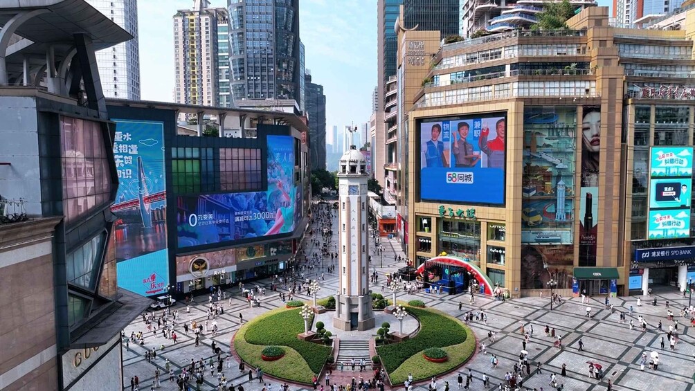 A busy urban square with a central monument, surrounded by modern buildings and large digital billboards. 4