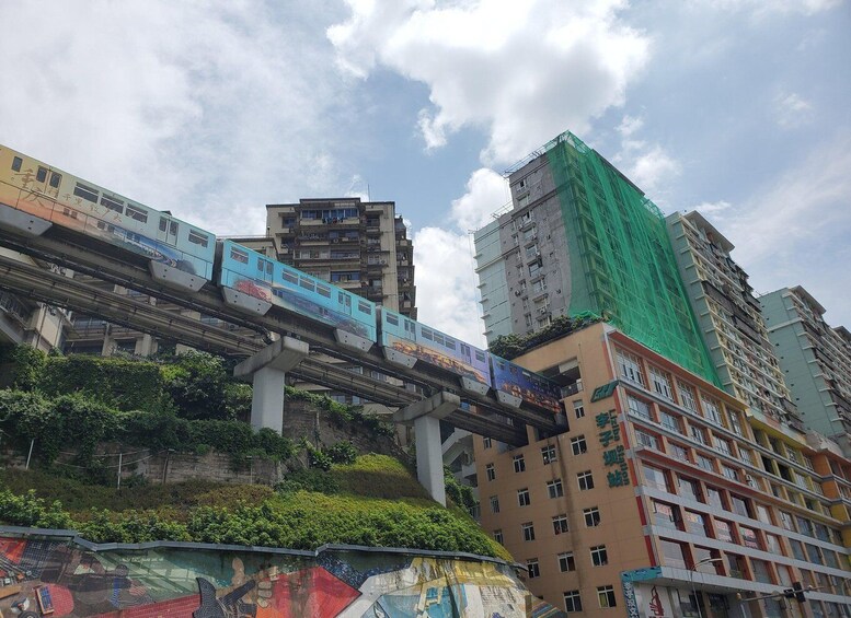 A blue train on an elevated track above a cityscape with buildings and greenery. 3
