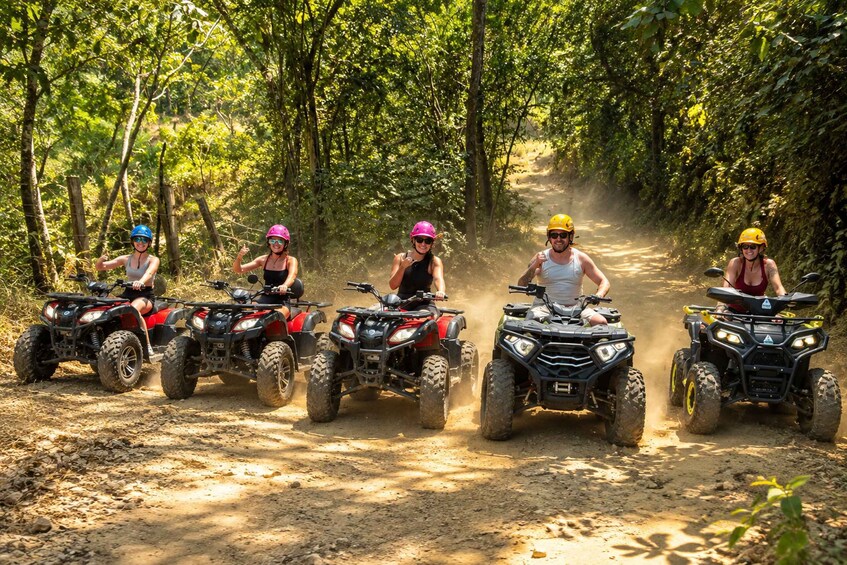 Four people riding ATVs on a dirt path surrounded by trees. 2