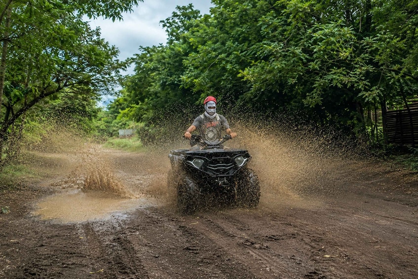A person riding an ATV on a muddy road surrounded by trees. 3