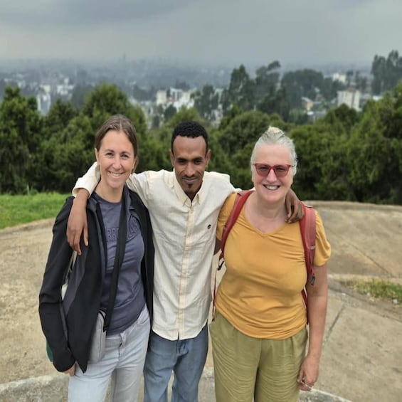 Three people standing on a concrete path with a cityscape in the background. 1